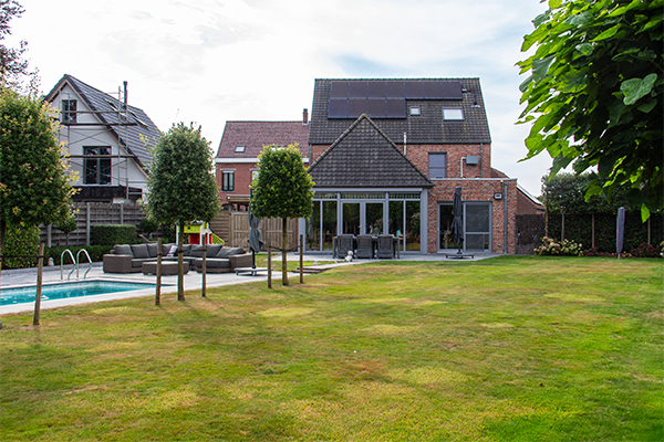 Achteraanzicht van villa met zonnepanelen, veranda, tuin en zwembad.