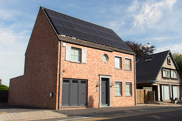Straatzijde van landelijke villa in baksteen met grijze ramen en garagepoort.